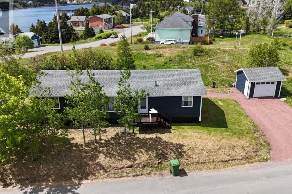 View from the side of a dark blue bungalow with a deck, detached garage and water in the background. - 1 Coady's Place, Marystown