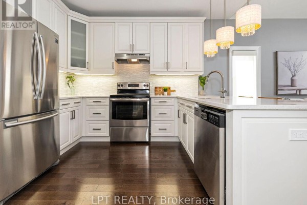 White kitchen with stainless steel appliances, quartz countertops, and dark wood floors. - 1 Dorchester Boulevard S, St  Catharines