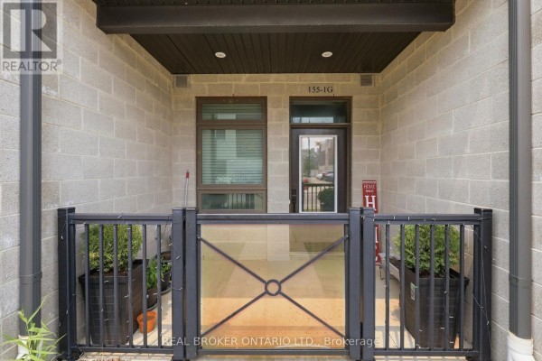 Close-up of townhouse entrance with concrete block walls, glass railing, and potted plants. - 1 G - 155 Thomas Slee Drive S, Kitchener