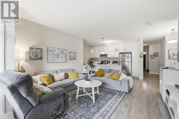 Living room with light grey sectional sofa, recliner, white coffee table, and open-concept kitchen. - 1 G - 155 Thomas Slee Drive S, Kitchener