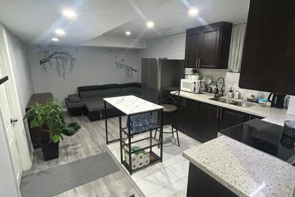 Open kitchen and living area with dark cabinetry, gray flooring, and a small island. - 1 Grape Trail, Brampton