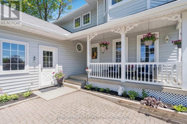 Covered front porch with a white door, glass panes, and two dark wicker chairs with blue cushions. - 1 Hallen Drive, Penetanguishene