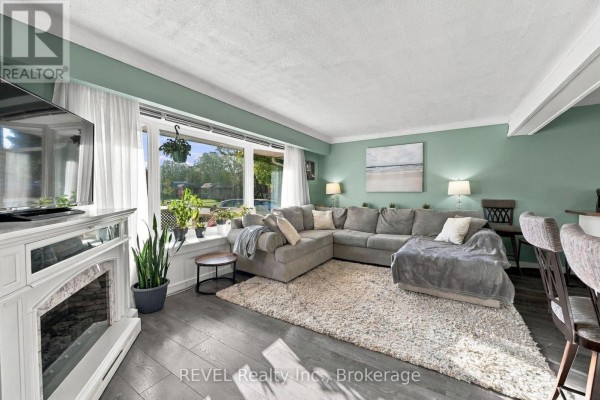 Open concept living and kitchen area with dining chairs, island stools, and wood beam. - 1 Idylwood Road, Welland