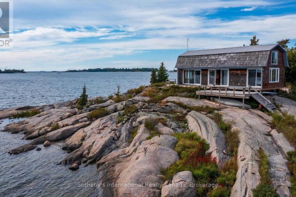 Wind-swept pine trees grow on a rocky outcrop along the water's edge under a blue sky. - 1 Island 352c, Carling