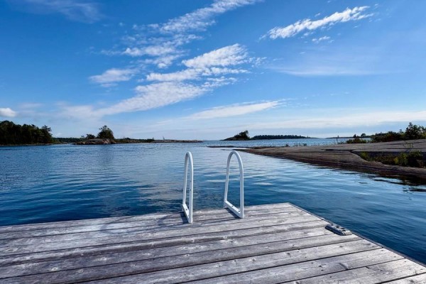 Small wooden cabin with large windows and a deck sits on a rocky island among trees. - 1 Island 352c, Carling