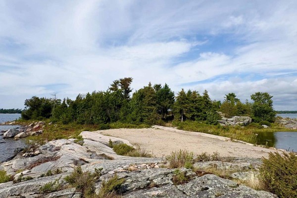 Rocky shoreline with sandy area and trees - waterfront property