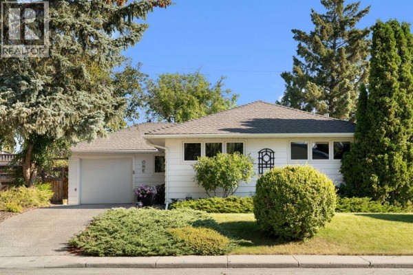 Side view of a white bungalow with large trees and bushes on the property. - 1 Kelwood Place Sw, Calgary