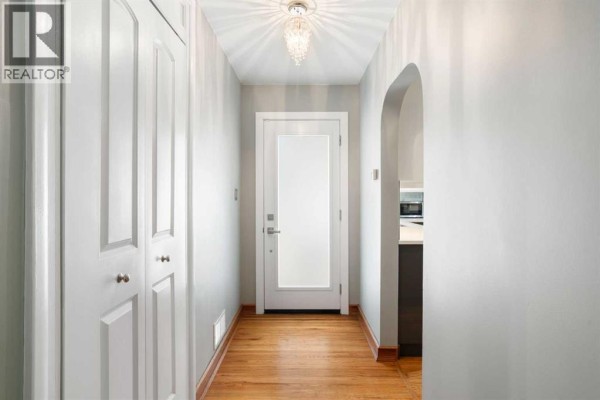 Interior hallway with grey cabinets, archway, hardwood floors, and a colorful abstract painting on the wall. - 1 Kelwood Place Sw, Calgary