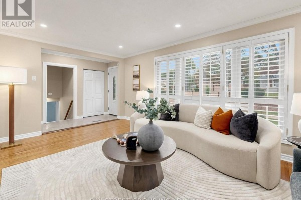 Living room with a curved cream sofa, hexagonal coffee table, and large window with shutters. - 1 Lesgay Crescent, Toronto