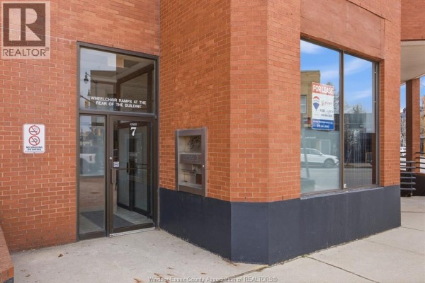Building entrance with double glass doors, brick exterior, and a "For Lease" sign on a large window. - 1 Main Street West Unit# 3, Kingsville