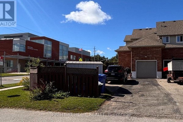 Rear view of townhouse with brick exterior, garage, and adjacent school building. - 1 Montgomery Boulevard, Orangeville