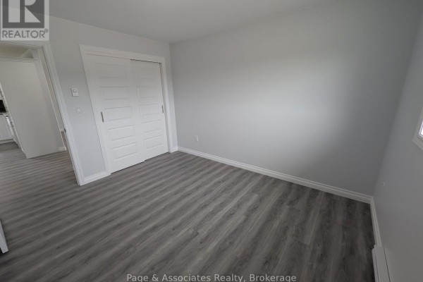 Empty bedroom with grey wood-look vinyl flooring, white baseboards, and white bi-fold closet doors. - 1 Moon Court, West Nipissing