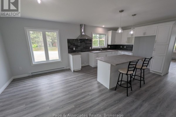 Spacious open-concept kitchen and living area with white cabinets, island, and grey laminate flooring. - 1 Moon Court, West Nipissing