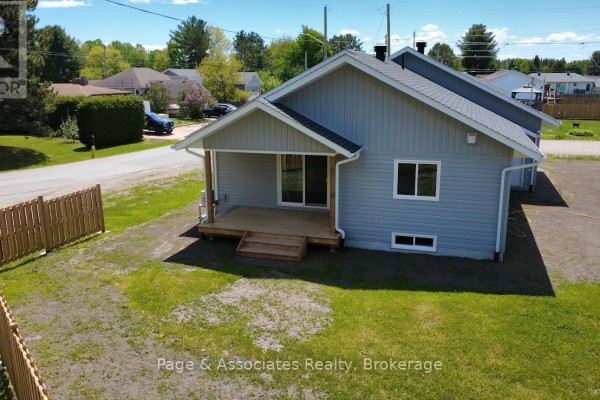 Rear exterior of a grey house with wooden deck, green lawn, and wooden fence. - 1 Moon Court, West Nipissing