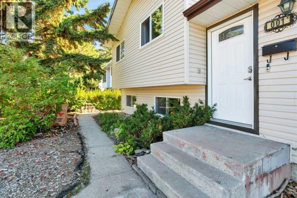 Close-up of the light beige siding and front door entrance with concrete steps. - 1 Mountain Place, Sylvan Lake