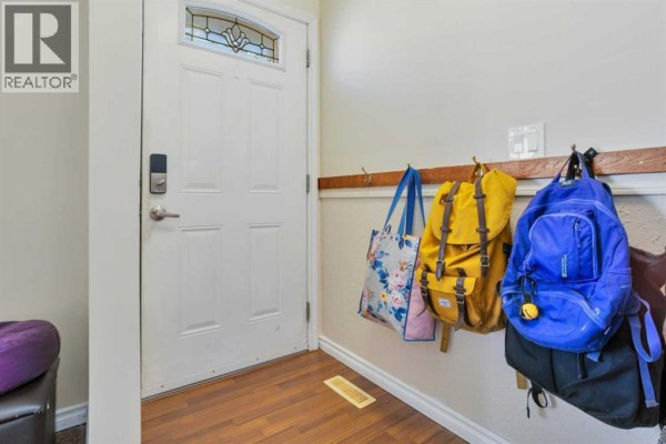 Interior view of a white front door with a stained-glass window and backpacks hanging on a wall rack. - 1 Mountain Place, Sylvan Lake