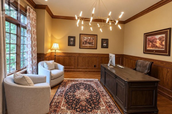 Home office with a large wooden desk, leather chair, two fabric armchairs, and a modern chandelier. - 1 Oakley Place, Toronto