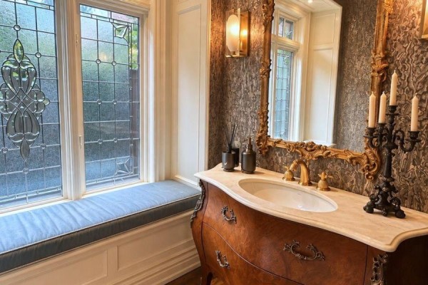Powder room with a vintage vanity, marble countertop, ornate mirror, and decorative glass window. - 1 Oakley Place, Toronto