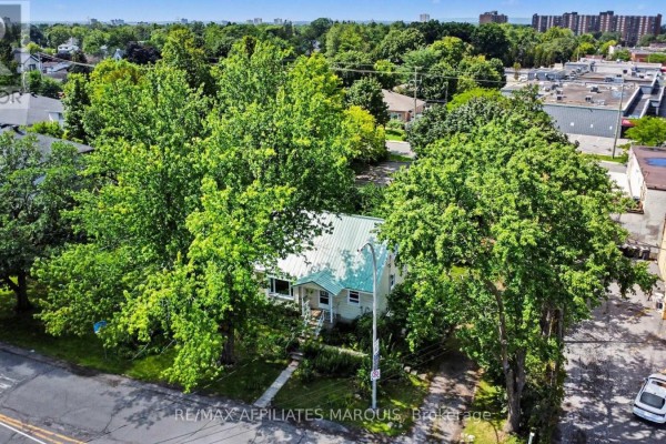 Aerial view of a yellow house with green metal roof surrounded by mature trees and suburban buildings. - 1 Withrow Avenue, Ottawa