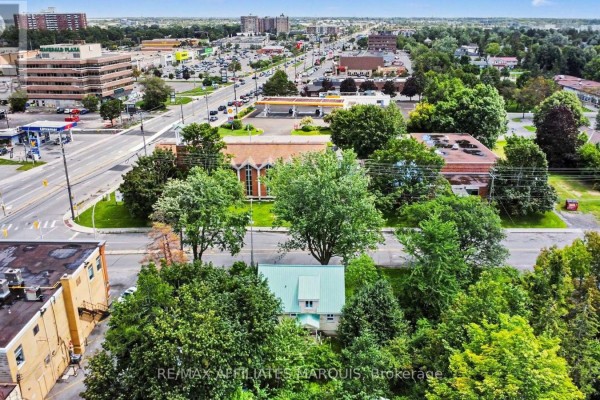 Aerial view showing the house and surrounding trees in the foreground with a commercial street scene in the background. - 1 Withrow Avenue, Ottawa