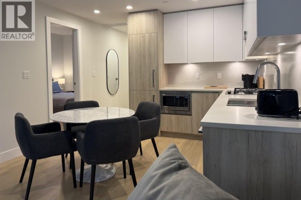 Open concept kitchen, dining, and living area with light wood floors and a patio door. - 1-bdrm 423 6th Street, West Vancouver