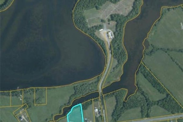 Aerial view of land parcels bordering a body of water, a road, and scattered buildings. - 1.5 Acres Route 117, Black River Bridge