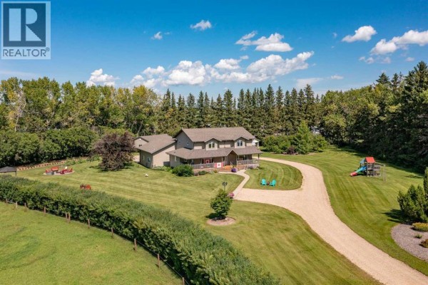 Front view of the house with a wraparound porch, visible deck, and play structures in the yard. - 10, 25028 Highway 595, Rural Red Deer County