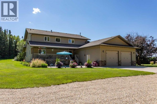 Side view of the house featuring a covered deck, large attached garage with three doors, and manicured lawn. - 10, 25028 Highway 595, Rural Red Deer County