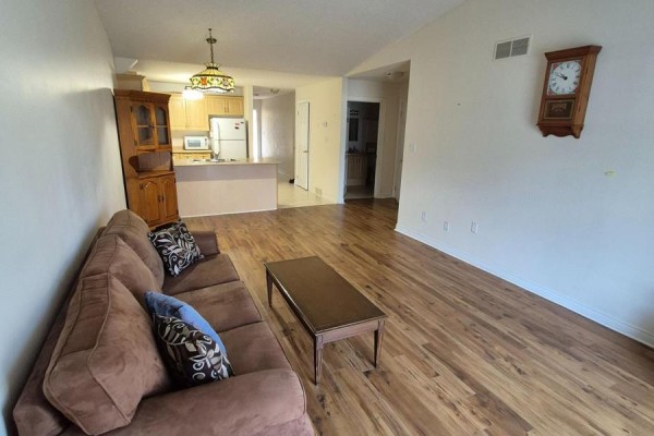 Living room with brown sofa, coffee table, and a view towards the kitchen and hallway entrance. - 10 - 162 First Street, Welland