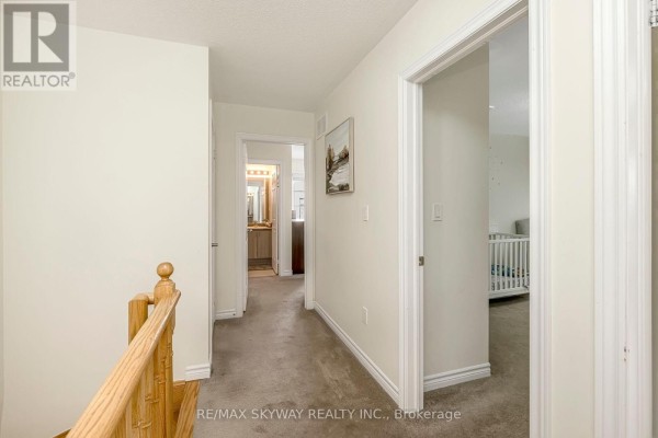 Hallway with wood railing, carpeted floor, and view into bathroom and nursery - 10 - 200 Veterans Drive Brampton