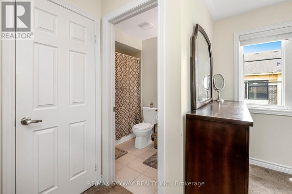 Bathroom with toilet, shower curtain, and tile floor; dresser and window visible - 10 - 200 Veterans Drive, Brampton