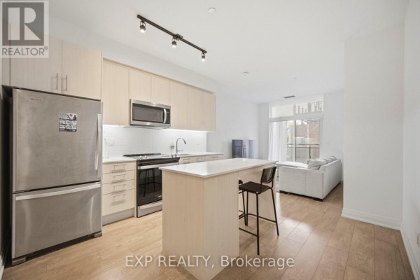 Open concept kitchen and living area with stainless steel appliances, light wood cabinets, and a white island. - 10 - 286 Main Street, Toronto