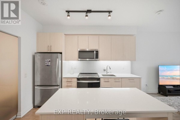 Modern kitchen featuring light wood cabinets, stainless steel appliances, a white island, and a television in the background. - 10 - 286 Main Street, Toronto