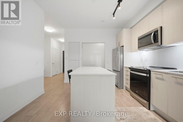 View of the kitchen island and surrounding area, showing light wood cabinets, stainless steel appliances, and hallway. - 10 - 286 Main Street, Toronto