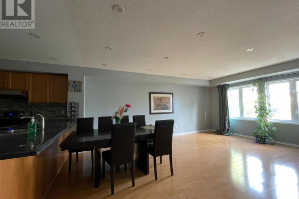 Dining area with dark wood table and chairs, adjacent to a kitchen island and living space. - 10 - 3375 Thomas Street, Mississauga