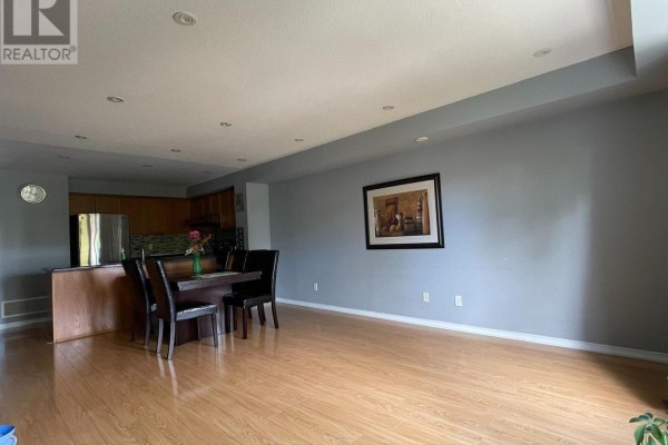 Open concept living and dining area with a kitchen island, dark wood table, and light wood floors. - 10 - 3375 Thomas Street, Mississauga
