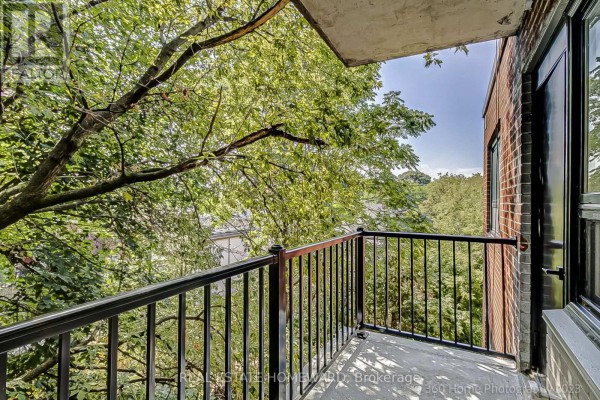 Balcony overlooking a lush green tree canopy with a metal railing and brick exterior. - 10 - 419 Woodbine Avenue, Toronto