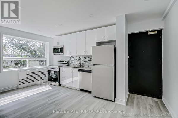 View of the modern kitchen with white cabinets, stainless steel appliances, and a large window. - 10 - 419 Woodbine Avenue, Toronto
