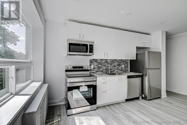 Close-up of the modern kitchen with stainless steel appliances, white cabinets, and a tiled backsplash. - 10 - 419 Woodbine Avenue, Toronto