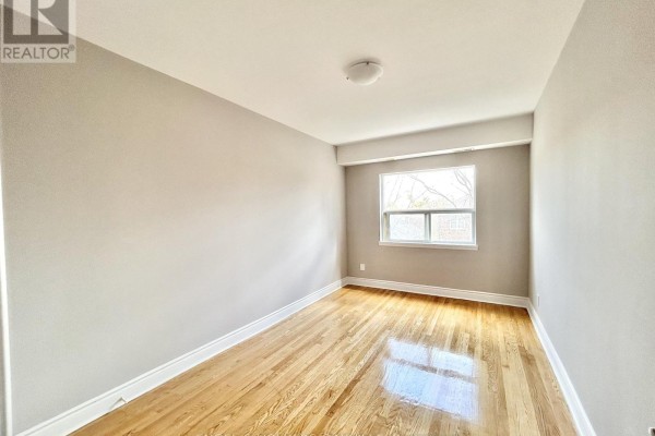 Empty bedroom with polished hardwood floors, neutral walls, and a window offering daylight. - 10 - 80 Twenty Fifth Street, Toronto