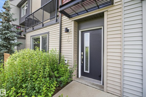 Close-up of a townhouse front door with a glass panel and beige siding. - #10 1075 Rosenthal Bv Nw, Edmonton