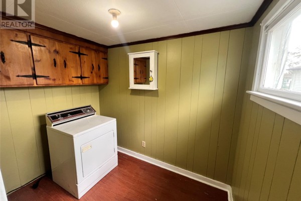 Laundry room with light green wood-paneled walls, a white dryer, and wood cabinetry overhead. - 10-12 Hill Avenue, Clarkes Beach