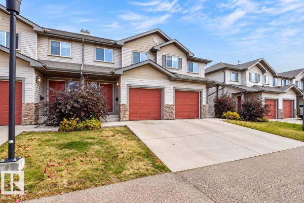 Exterior view of townhouse complex with light gray siding and red garage doors. - #10 2816 34 Av Nw Nw, Edmonton
