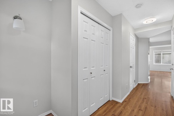 Interior hallway with wood laminate flooring, white bi-fold closet doors, and light gray walls. - #10 2816 34 Av Nw Nw, Edmonton