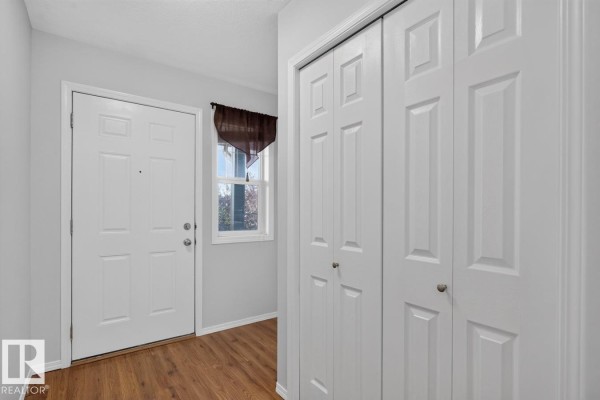 Interior entryway with a white front door, window, wood laminate floor, and closet doors. - #10 2816 34 Av Nw Nw, Edmonton