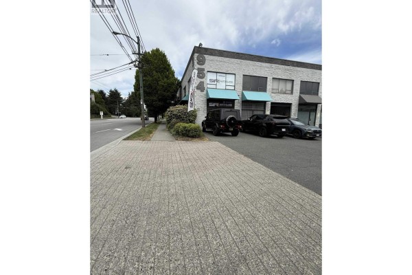 Sidewalk view of a grey commercial building at 954 Marine Drive, Vancouver, with parked cars and trees. - 10 954 Sw Marine Drive, Vancouver