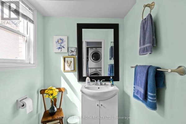 Powder room with light green walls, a white vanity, a black framed mirror, and stacked washer and dryer visible. - 10 Andrea Crescent, Orillia