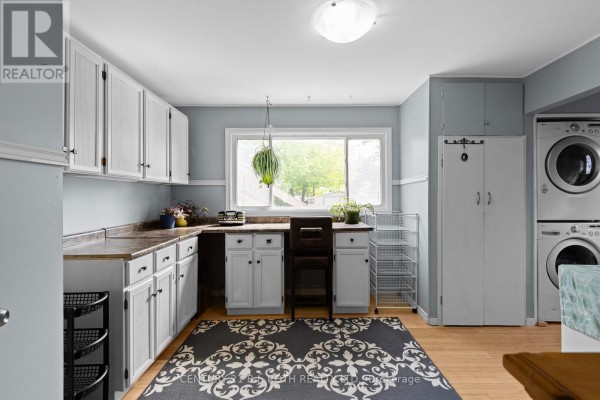 Laundry room with white cabinetry, laminate countertops, a stacked washer and dryer, and a large window view. - 10 Andrea Crescent, Orillia