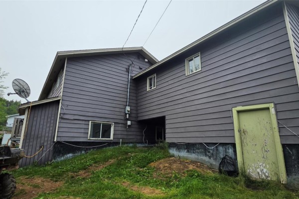 Rear exterior of the apartment building showing dark siding, windows, and an old green door. - 10 Atlantic Street, Marystown