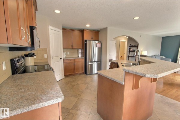 Kitchen with light brown cabinets, stainless steel refrigerator, granite countertop island, and an archway to the living room. - 10 Birchmont Cr, Leduc